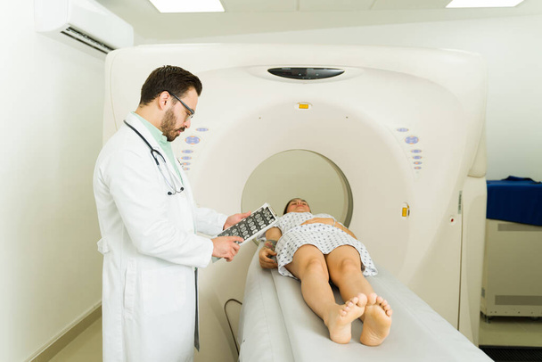 Professional radiologist checking the scan diagnostic of a young woman getting a computed tomography at the medical imaging center - Photo, Image