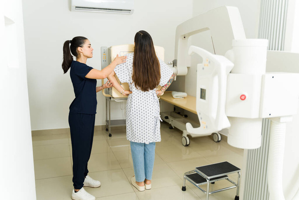 Οπίσθια όψη γυναίκας ακτινολόγου ή νοσοκόμου που βοηθά ασθενή ασθενή να κάνει ακτινογραφία θώρακος στο εργαστήριο διαγνωστικής απεικόνισης - Φωτογραφία, εικόνα