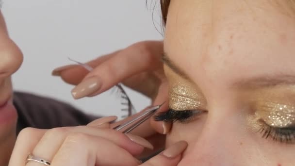 Beautiful bright professional makeup in a beauty studio. Make-up artist glues artificial long eyelashes to give expressiveness to the eyes, close-up view. - Footage, Video