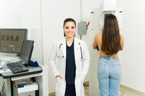 Επαγγελματική γυναίκα γιατρός χαμογελά, ενώ κάνει μια μαστογραφία σε μια νεαρή γυναίκα για την πρόληψη του καρκίνου του μαστού στο εργαστήριο ιατρικής απεικόνισης - Φωτογραφία, εικόνα