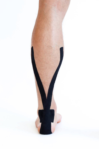 Kinesiologia trattamento nastro con nastro nero sul paziente maschio ferito tendine d'Achille. Trattamento kinesio infortunio sportivo. - Foto, immagini