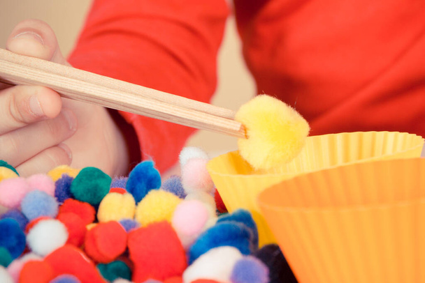 Preschooler playing with small colorful pompoms, wooden tongs and cups. Development of kids motor skills, coordination, creativity and logical thinking - Foto, Bild