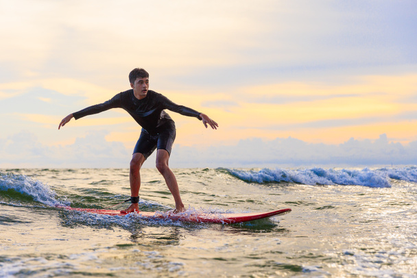 Young teen boy surfer riding waves on soft board in Rayong beach, Thailand. Rookie teenager surfboard student playing on water in excited and funny action. Sports teenagers practice surfing lessons. - Foto, imagen