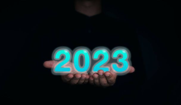 Сияющий и светящийся синий календарь 2023 года. Цифры 2023 года на руках бизнесмена на темном фоне для цифровой и технологической концепции. Поздравляем с Рождеством и Новым годом!. - Фото, изображение