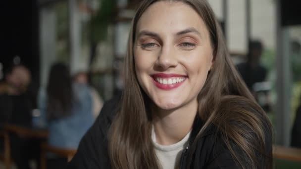 Portrait d'une charmante jeune femme souriante devant une caméra assise au café. Fille heureuse dans 20s sourire - Séquence, vidéo