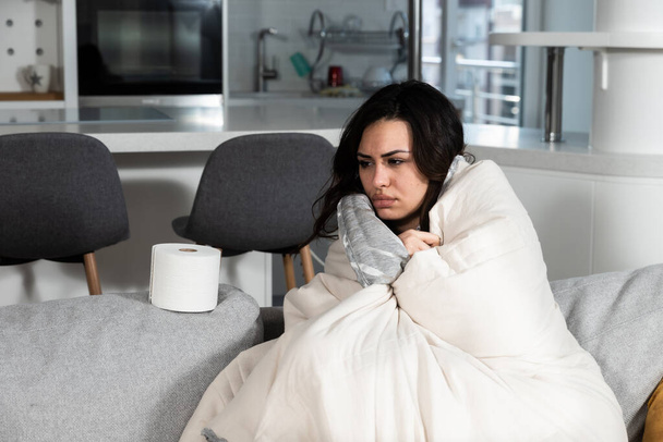 Young sick stressed woman lying at home covered with blanket blowing her nose. Ill female have common cold and flue with runny nose allergy reaction wipe it with paper tissue. - Fotó, kép