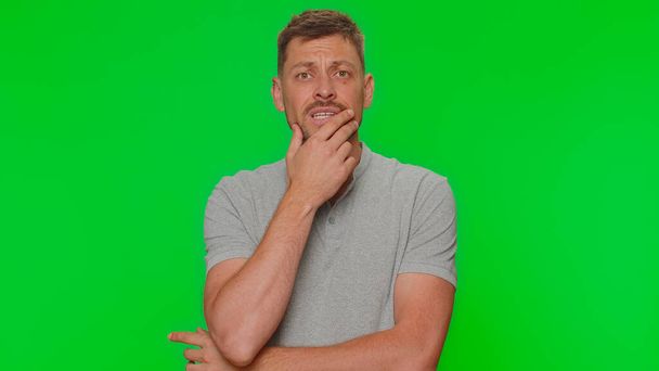 Bearded young man feeling hopelessness and loneliness, nervous breakdown, loses becoming surprised by lottery results, bad fortune, loss, unlucky news. Adult guy on green chroma key studio background - Photo, image
