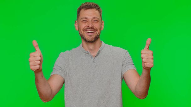 Like. Bearded handsome young man raises thumbs up agrees with something or gives positive reply recommends advertisement likes good. Adult guy isolated alone on chroma key studio background indoors - 写真・画像
