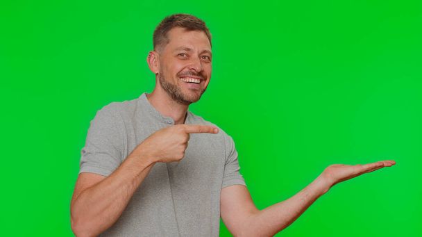 Bearded handsome young man showing thumbs up and pointing right empty place, advertising area for commercial text, copy space for goods promotion. Adult guy isolated on chroma key studio background - Fotografie, Obrázek