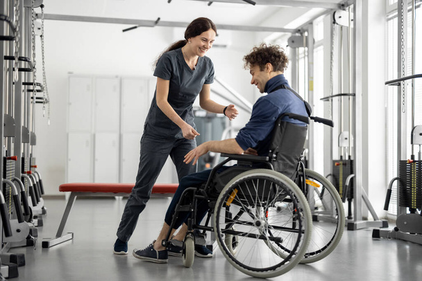 Rehabilitasyon uzmanı rehabilitasyon merkezinde bir adamın tekerlekli sandalyeden kalkmasına yardım ediyor. Fizik tedavi kavramı ve engelli insanlara destek - Fotoğraf, Görsel