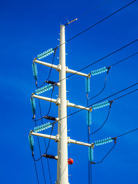 Close-up of the top of a white high voltage electrical pole against a blue sky, black electrical wires, fuses, sunny day, viewed from a low angle perspective - Fotoğraf, Görsel