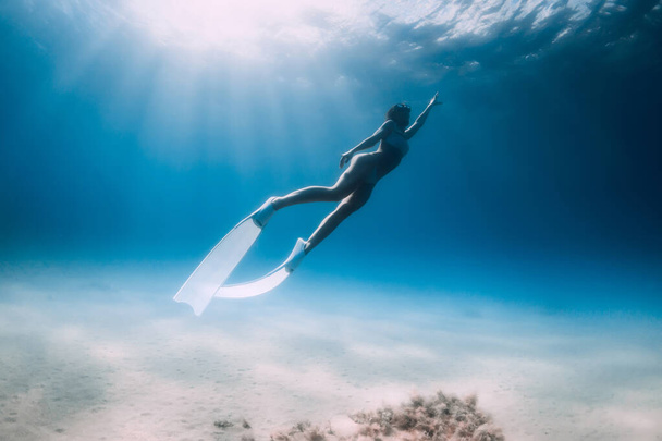 Attractive lady freediver underwater glides with white fins in blue ocean with sun rays - Fotografie, Obrázek
