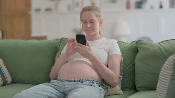 Pregnant Young Woman Browsing Smartphone while Sitting on Sofa - Video, Çekim