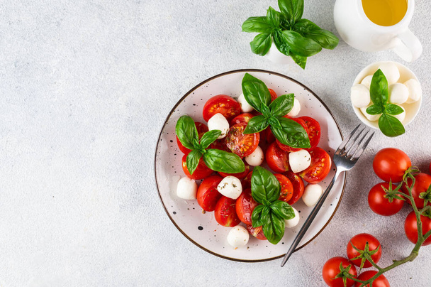 Italian caprese salad with sliced tomatoes, mozzarella, basil, olive oil on a light background. Top view. Italian food. Healthy salad. Summer food. - Foto, afbeelding