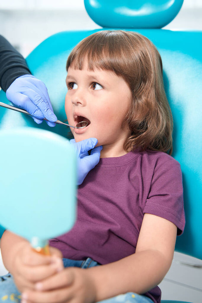 Dental professional in nitrile gloves performing examination of oral cavity of young female patient - Photo, image