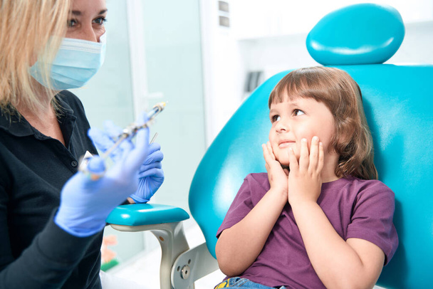 Frightened little girl looking at pediatric dentist with dental syringe in hands - Foto, Imagem