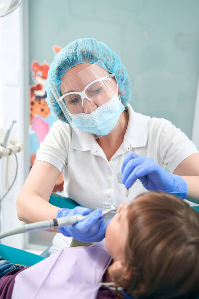 Focused pediatric dentist in nitrile gloves and face mask treating child teeth - Fotó, kép