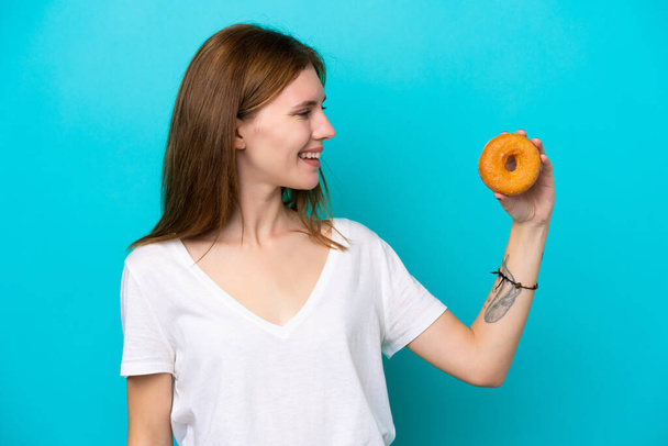 Young English woman holding a donut over isolated blue background with happy expression - Foto, Bild