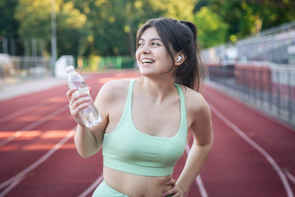 Attractive young woman in sportswear with a bottle of water on a jog in the stadium. - Foto, Imagem