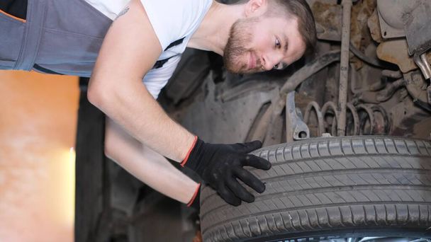 Dikey video, profesyonel bir araba tamircisi bir araba tamirhanesinde kaldırma makinesinin kralı altında çalışıyor. Araba servisi, elektrikli arabaların tamiri. - Fotoğraf, Görsel