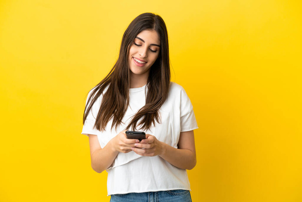 黄色の背景に隔離された若い白人女性携帯電話でメッセージを送る - 写真・画像
