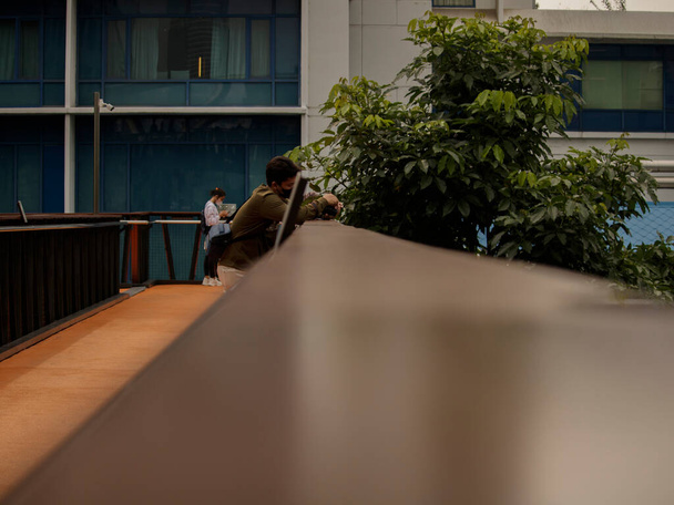 Jakarta, Indonesien - 27. August 2022: Geschäftsmann und Coronavirus-Epidemie. Nahaufnahme Porträt eines jungen Geschäftsmannes mit Einweg-Gesichtsmaske. Ein Mann wehrt sich gegen eine 19-Jährige auf der Großstadtstraße. Moderne Gebäude im Hintergrund - Foto, Bild