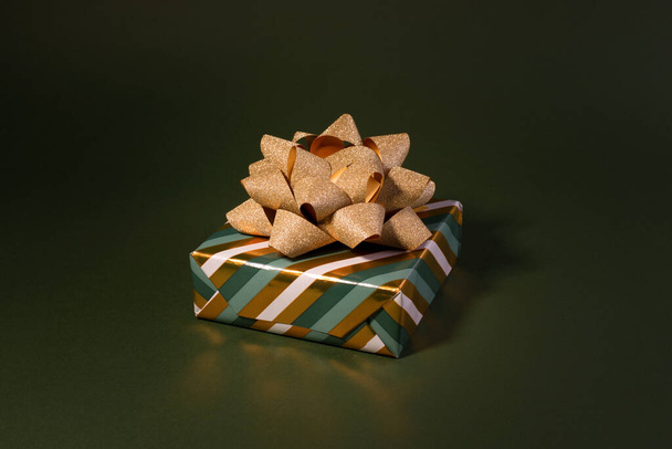 Boxing Day concept με κουτιά δώρου σε χρυσές και πράσινες ρίγες διακοσμημένο με αφρώδη φιόγκο σε φόντο πράσινου χρώματος. - Φωτογραφία, εικόνα