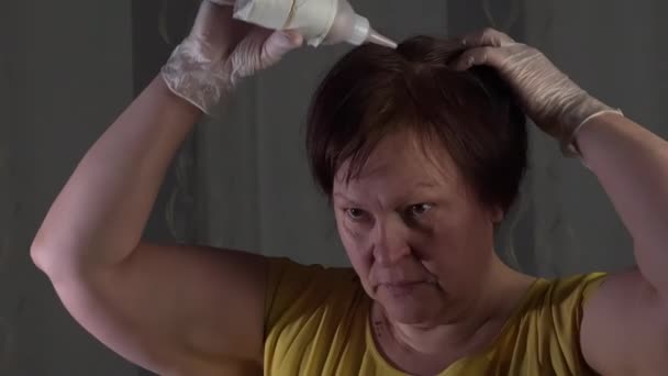 Caucasian lady styling her hair. White rubber gloves. Yellow shirt. White and gray background. Middle-aged. Red hair. Using hair dye. Camera slowly moving around. - Filmati, video