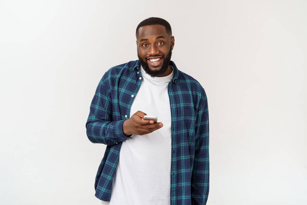 Smiling African American young man holding phone looking at smartphone isolated on white grey studio background - Foto, Imagen