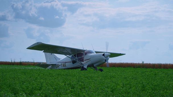 Lightweight airplane standing green field with working propeller preparing to flight. Small private plane with spinning blades parked on grass airfield. View of modern aircraft in front beautiful sky. - Photo, image