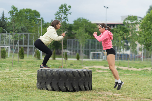 One girl is jumping on the big bulldozer tire while the other is wwaiting her while squatting - Fotoğraf, Görsel
