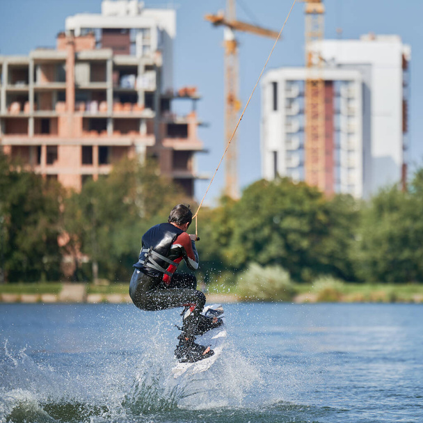 Wakeboarder surfing on lake. Young man surfer having fun wakeboarding in the cable park. Water sport, outdoor activity concept. - Photo, Image