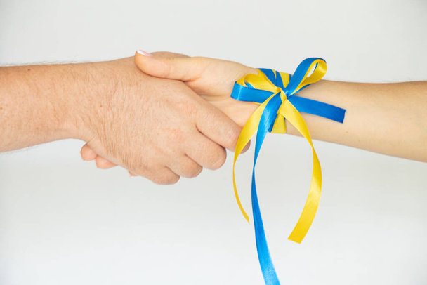 Handshake of a man and a woman with a ribbon on the hand of the flag of Ukraine on a white background, partnership and union of two partners, the flag of Ukraine on the hand of a girl - Valokuva, kuva