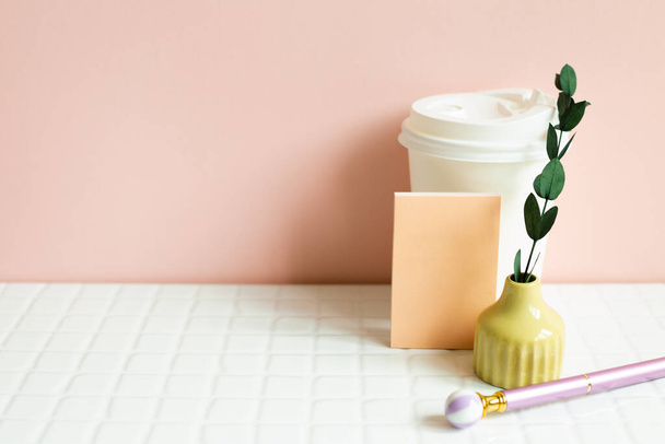 Paper coffee cup, memo pad, pen, dry plant on white desk. pink wall background - Foto, imagen