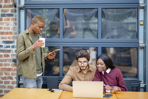Multiracionális diákok videohívása laptopon a szabadban. A távoktatás és az e-tanulás fogalma. A diákok életmódjának ötlete. Mosolygó fiatal indiai férfi, fekete lány és srác. Egyetemi campus - Fotó, kép