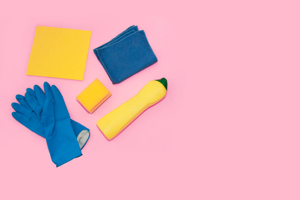 household supplies for cleaning the apartment, blue gloves, yellow foam sponge, cleaning cream in a bottle, on a pink background, top view - Foto, imagen