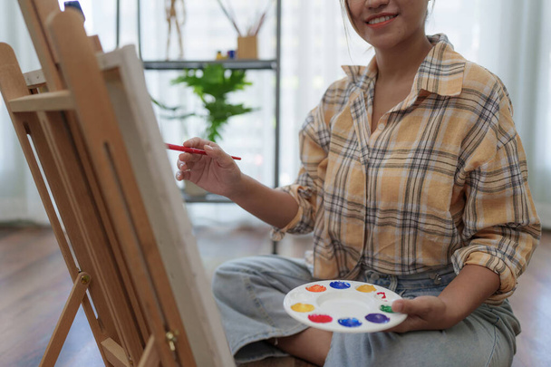 Joyful young female artist painting on canvas at workshop. - Zdjęcie, obraz