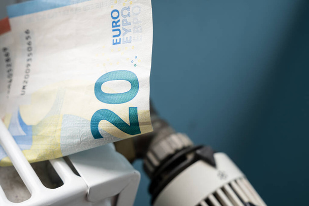ラジエーターとサーモスタット・ノブのユーロ紙幣は、灰色の壁に対して、最小限でクローズアップされます。エネルギー危機と高価な加熱コストの概念. - 写真・画像