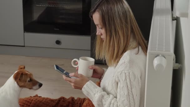 Worried sad woman sits under blanket near heating radiator and use smartphone, Rising costs in private households for gas bill due to inflation and war, Energy crisis - Filmagem, Vídeo