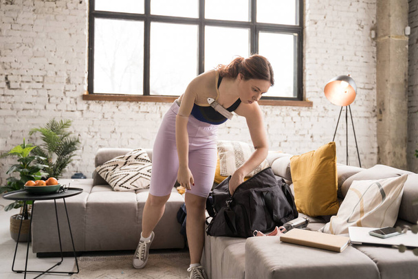 Full length view of the female with artificial hand packing her bag at home while preparing to the training. Sport and people concept. Stock photo - Photo, Image