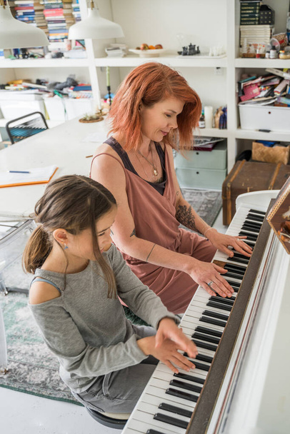 Вертикальный вид молодой женщины, играющей за фортепиано и изучающей свою маленькую дочь дома. Музыка и хобби. Фото на складе - Фото, изображение
