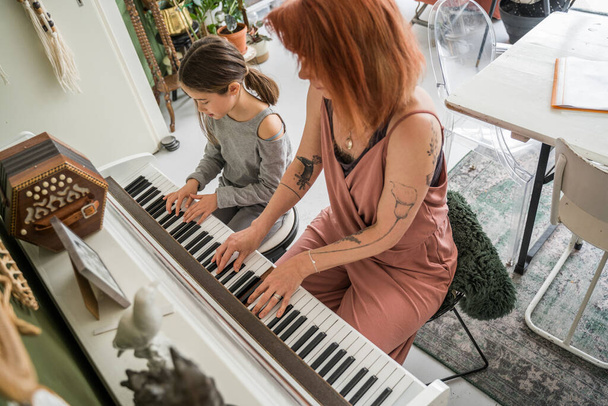 Caucasian woman sitting at the piano and playing song together with her little daughter. Family and maternity concept. Stock photo - Foto, Imagen