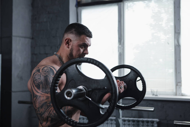 Huge tattooed muscular man working out with barbell, doing biceps curls - Foto, immagini