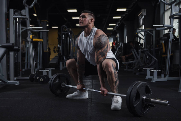 Full length shot of a huge muscular tattooed fitness man working out with barbell at gym - Fotoğraf, Görsel
