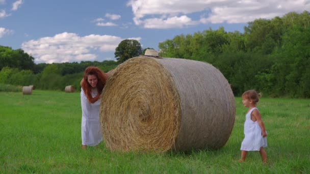 Mom and daughter in white dresses in the field. Straw stacks stack bales of hay left over from harvesting crops. Landscape of straw bales against setting sun on background. High quality 4k footage - Footage, Video