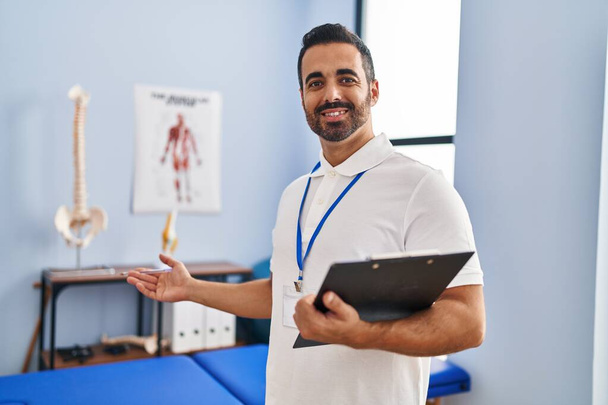 Young hispanic man physiotherapist smiling confident holding clipboard at rehab clinic - Photo, Image