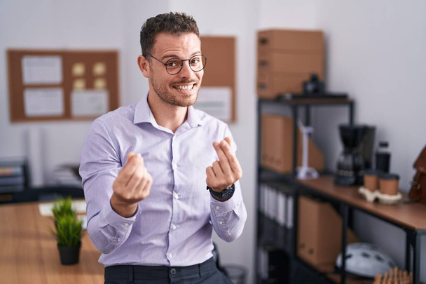 Young hispanic man at the office doing money gesture with hands, asking for salary payment, millionaire business  - Photo, Image