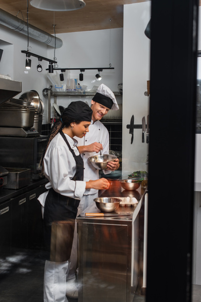 cheerful multiethnic chefs cooking together in professional kitchen  - Fotografie, Obrázek