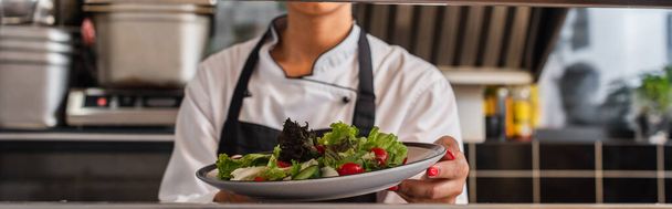 cropped view of african american chef holding plate with freshly cooked salad in professional kitchen, banner - Fotoğraf, Görsel