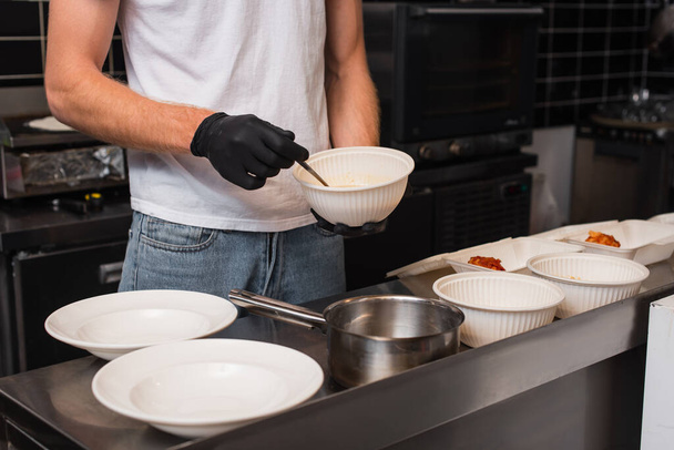 cropped view of volunteer in latex gloves holding plastic bowl in kitchen  - Fotó, kép